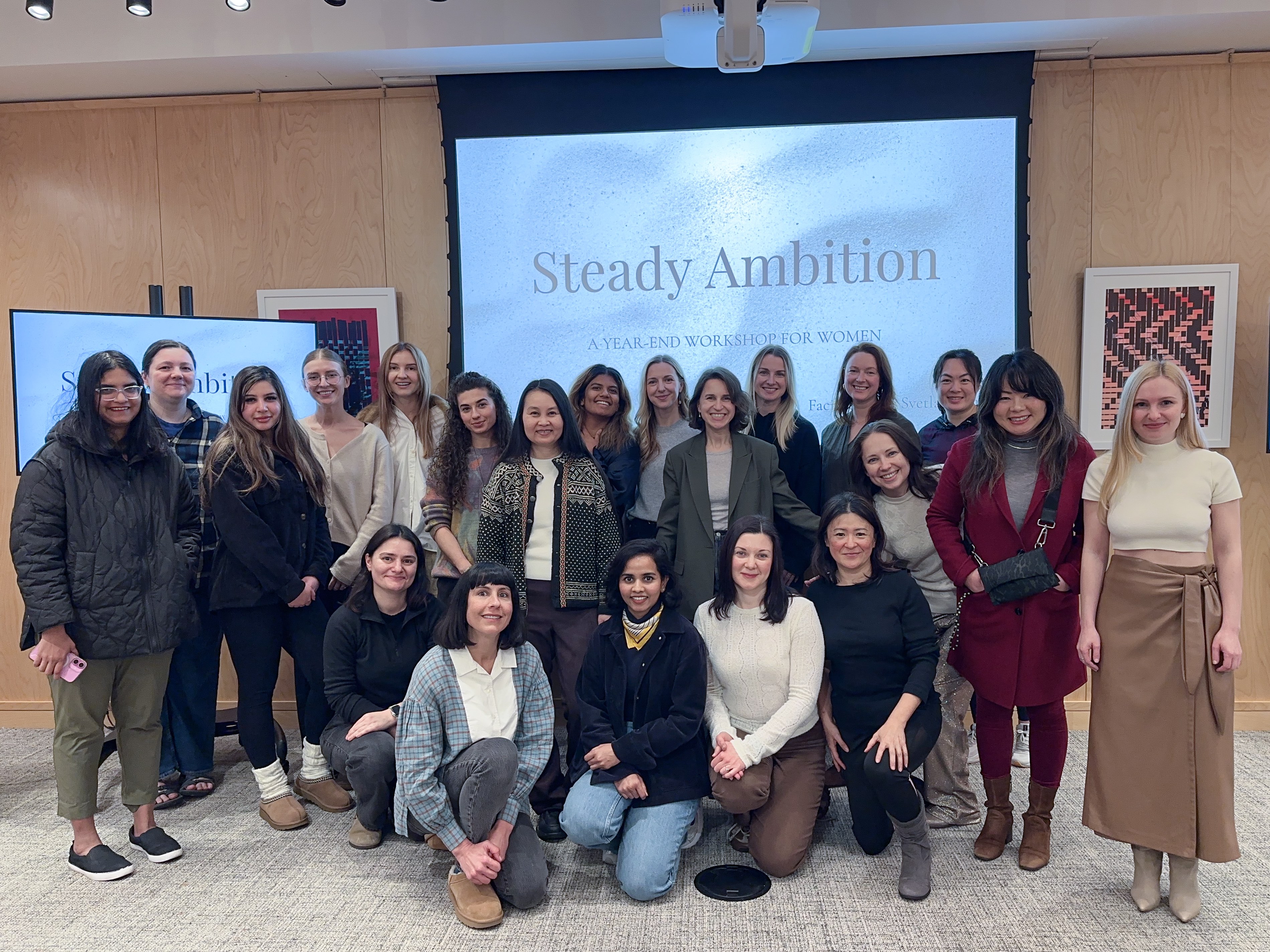 A group of women gathered together at the Steady Ambition year-end workshop in front of a screen reading Steady Ambition, A Year-End Workshop for Women.